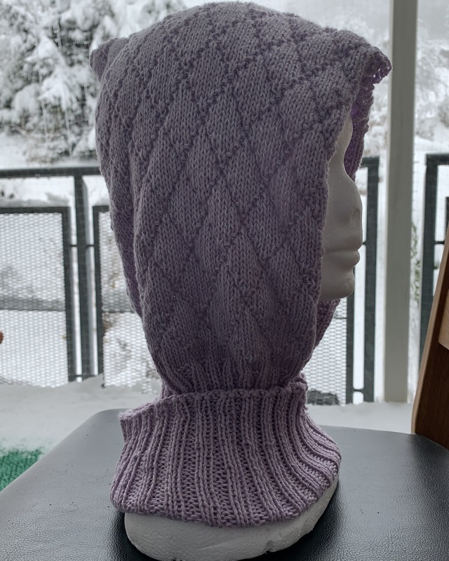 Helllila gestrickte Kapuze mit Rautenmuster und hohem Rippenkragen auf Schaufensterpuppe vor verschneitem Balkon