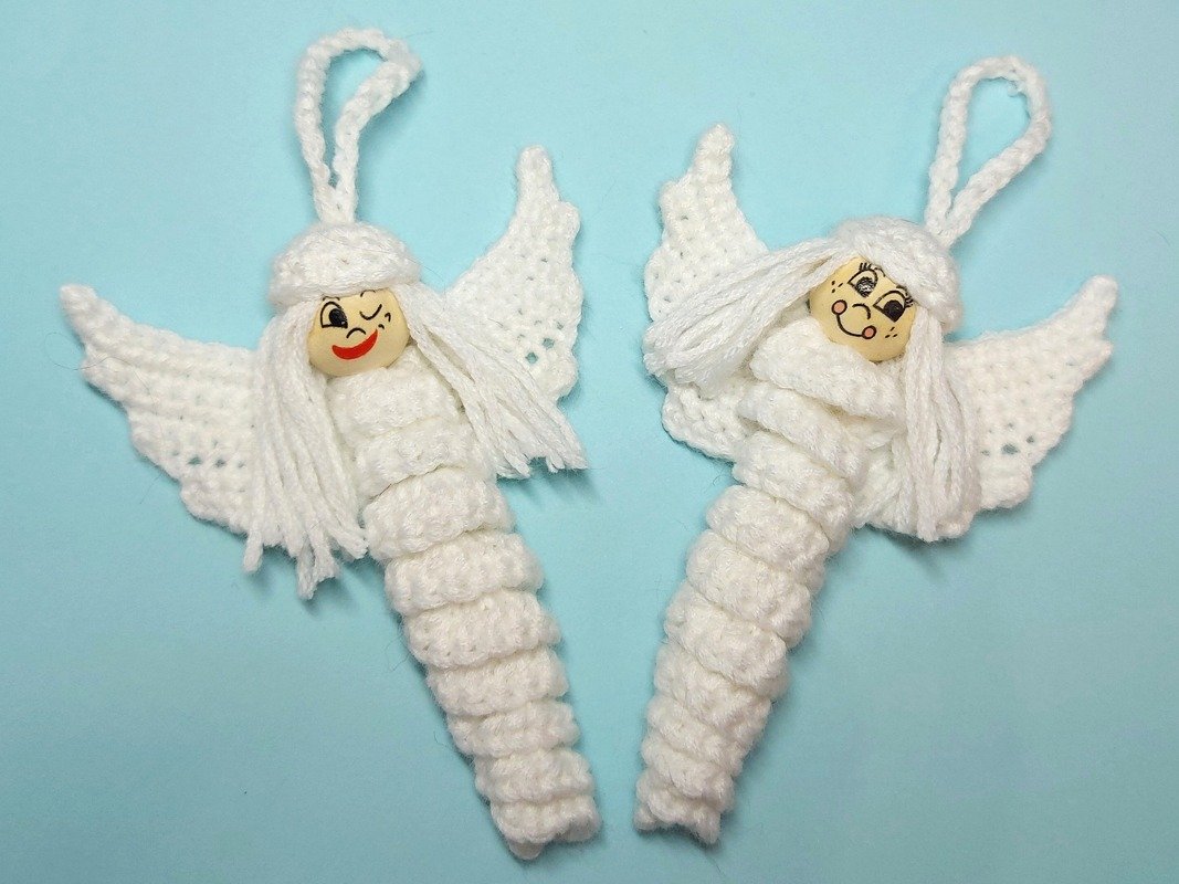Zwei weiße gehäkelte Engel-Anhänger mit Holzperlenköpfen und Aufhängeschlaufen auf hellblauem Hintergrund