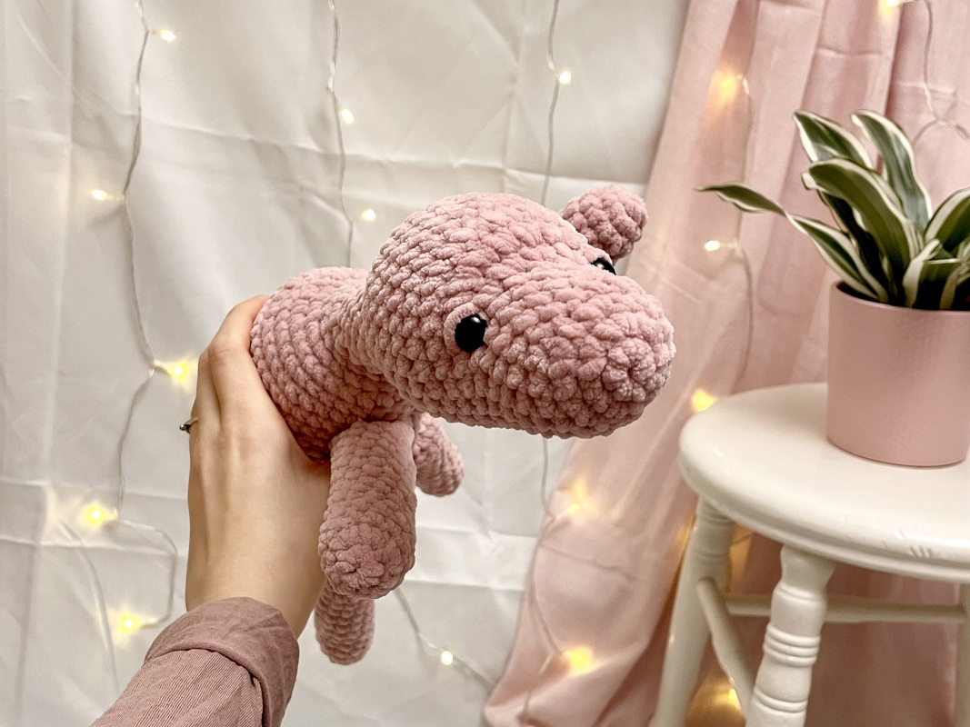 Nahaufnahme eines rosa Amigurumi‑Dinos mit Hand zur Größenangabe