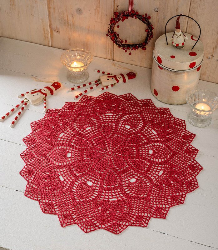 Rotes rundes Häkeldeckchen auf weißem Tisch mit Kerzen und Weihnachtsdekoration