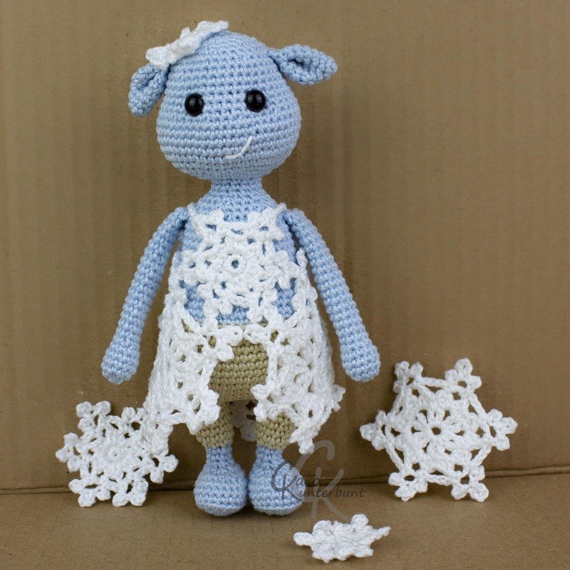 hellblaues Amigurumi-Lamm mit weißem Spitzencape und gehäkelten Schneeflocken