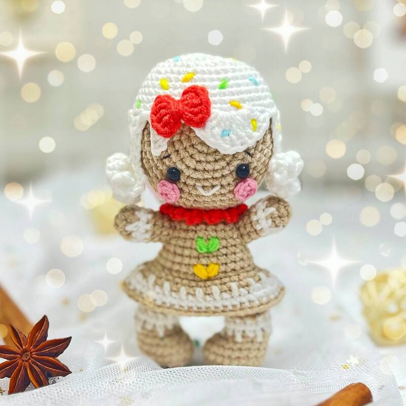 Crochet gingerbread amigurumi doll with white icing cap, red bow and pink cheeks