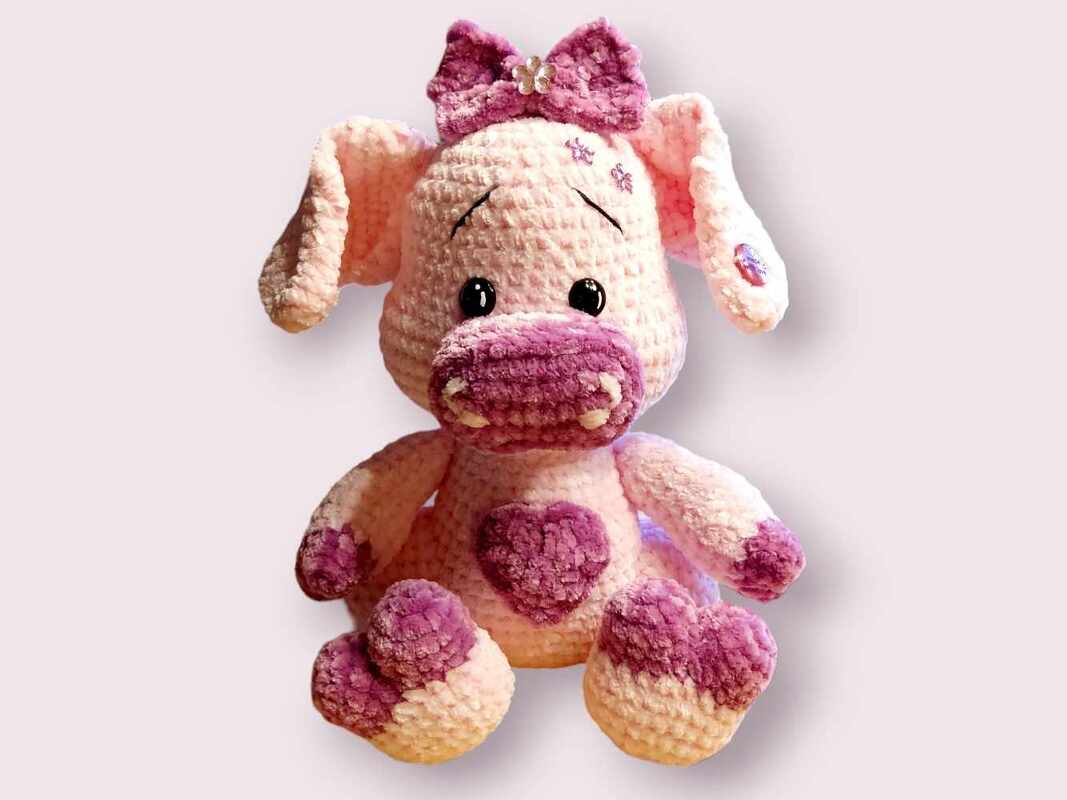 Zartes rosa Amigurumi-Schwein mit lila Herz und Schleife am Kopf