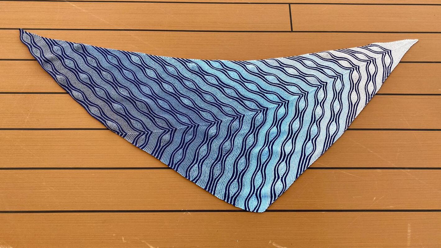Dreieckstuch gestrickt mit blau-weißem Wellenmuster auf Holzuntergrund