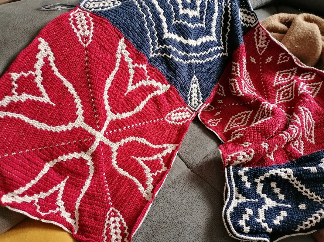 gehäkelte Decke aus roten und blauen Quadraten mit weißen Mustern auf Sofa