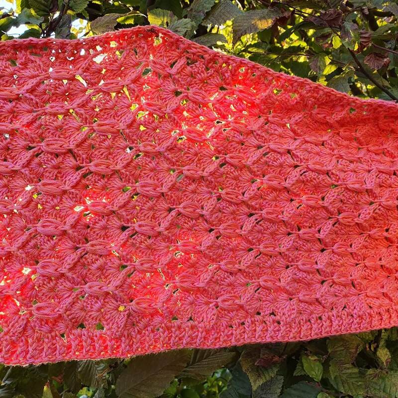 Nahaufnahme eines korallfarbenen geh
elten Schals mit schlaufigem Lochmuster