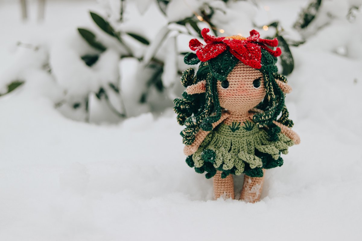 Gehäkelte Amigurumi-Puppe mit grünem Kleid und roter Blütenhaube im Schnee