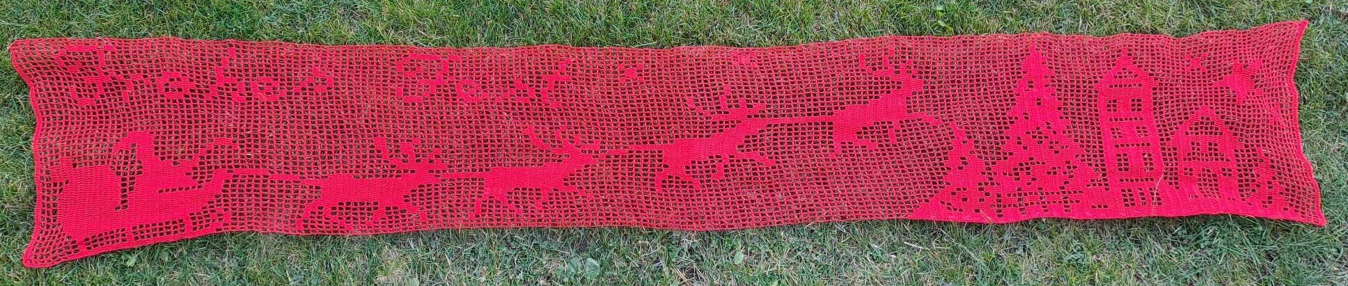 Roter gehäkelter Tischläufer mit Rentiermotiv auf Gras, Draufsicht