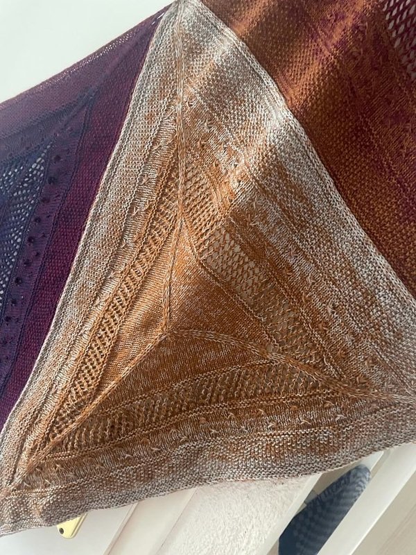Three overlapping knitted shawls; foreground triangular brown-orange lace and textured shawl.