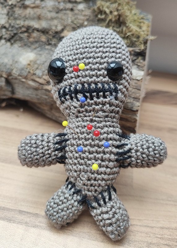 Gehäkelte graubraune Amigurumi-Puppe mit schwarzen Sicherheitsaugen und bunten Stecknadeln