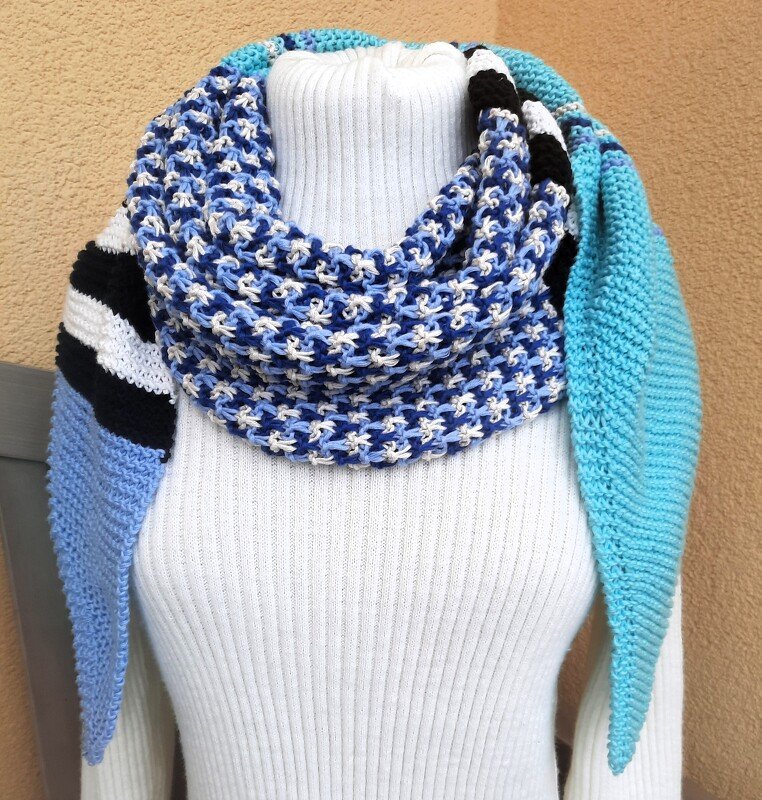 Mehrfarbiges gestricktes Tuch in Blautönen, Weiß und Schwarz mit gestreiften und gemusterten Abschnitten, um eine Schaufensterpuppe mit weißem Rollkragenpullover drapiert.
