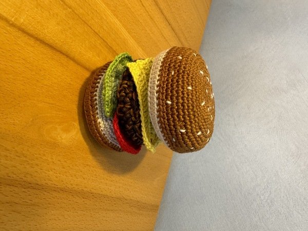 Bunter gehäkelter Burger mit Sesambrötchen und Schichten aus Salat, Tomate und Patty