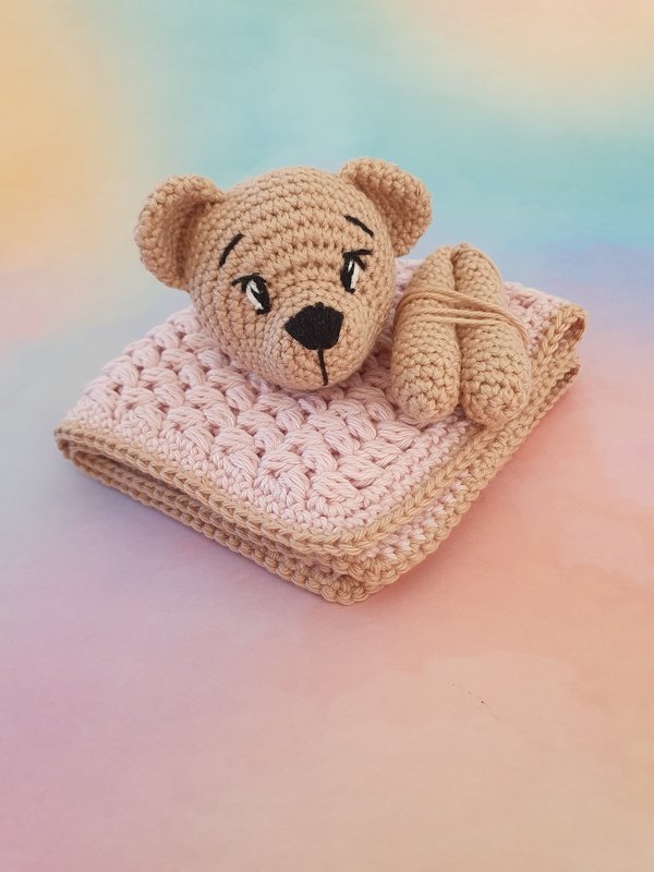 Pink shell-stitch crochet baby blanket folded with a tan crocheted teddy head and matching paws