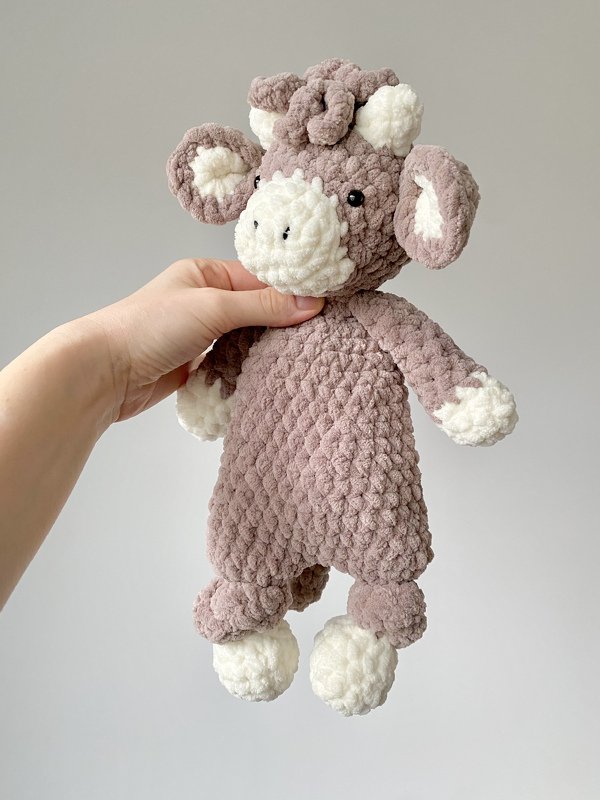 Hand holding a mauve and white crocheted calf plush made from chunky textured yarn.