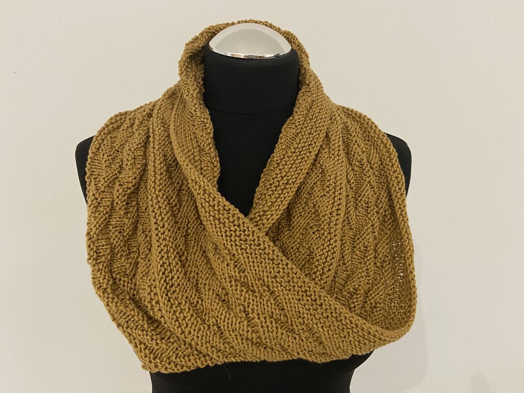 Senfgelber gestrickter Loop-Schal mit Strukturmuster auf schwarzer Schneiderbüste vor hellem Hintergrund.