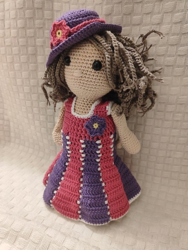 Gehäkelte Amigurumi-Puppe mit lila Hut, pinker Blüte und gestreiftem Kleid in Pink und Lila