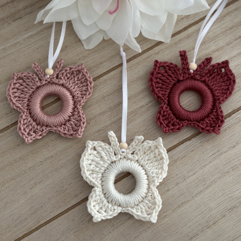 Zarte gehäkelte Schmetterlingsanhänger in Rosa, Creme und Dunkelrot mit weißen Bändern und Holzperlen