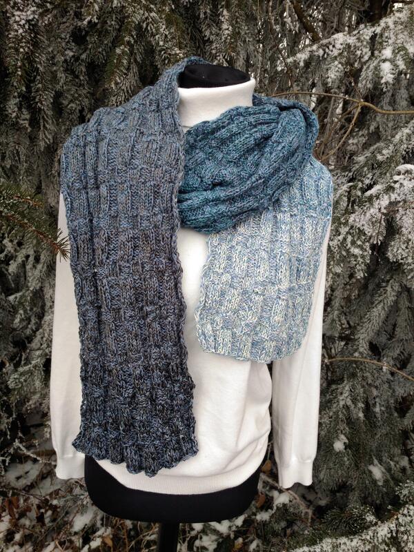 Gestrickter blau-grüner Schal mit Kästchenmuster auf einer Büste vor verschneiten Tannenzweigen