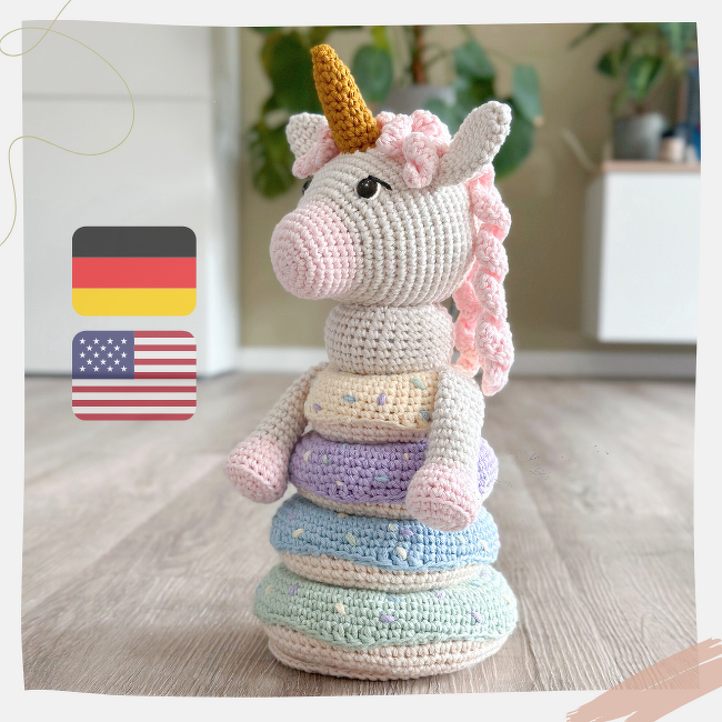 Amigurumi unicorn head on top of removable pastel crochet rings stacked on a wooden floor