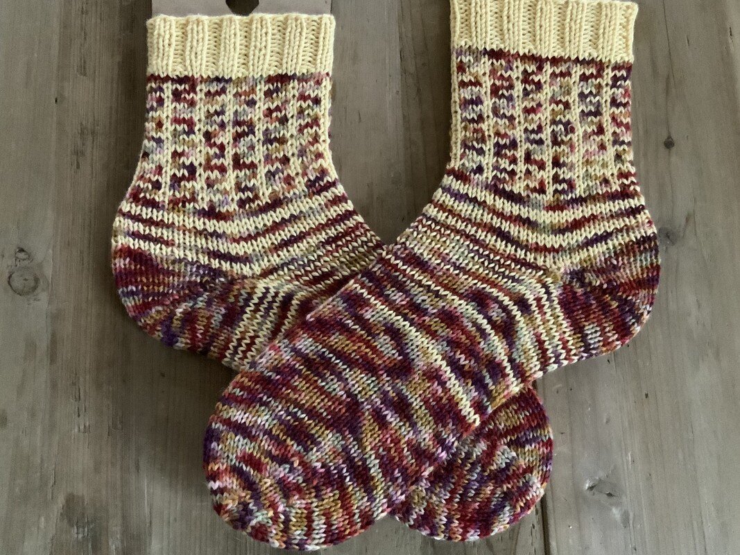 Handgestrickte mehrfarbige Socken mit cremefarbenem Bündchen auf Holztisch
