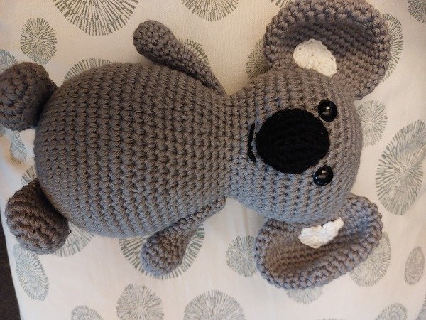 Nahaufnahme eines grau gehäkelten Koala-Amigurumi mit angenähten Ohren und schwarzer Nase
