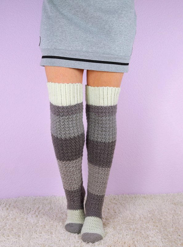 Gestreifte gehäkelte Overknee-Socken in Grau und Creme an Damenbeinen