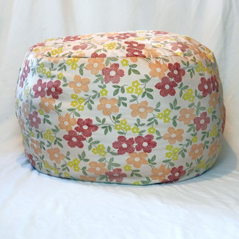 Runder Pouf mit sichtbaren Nähten und geblümtem Stoffbezug