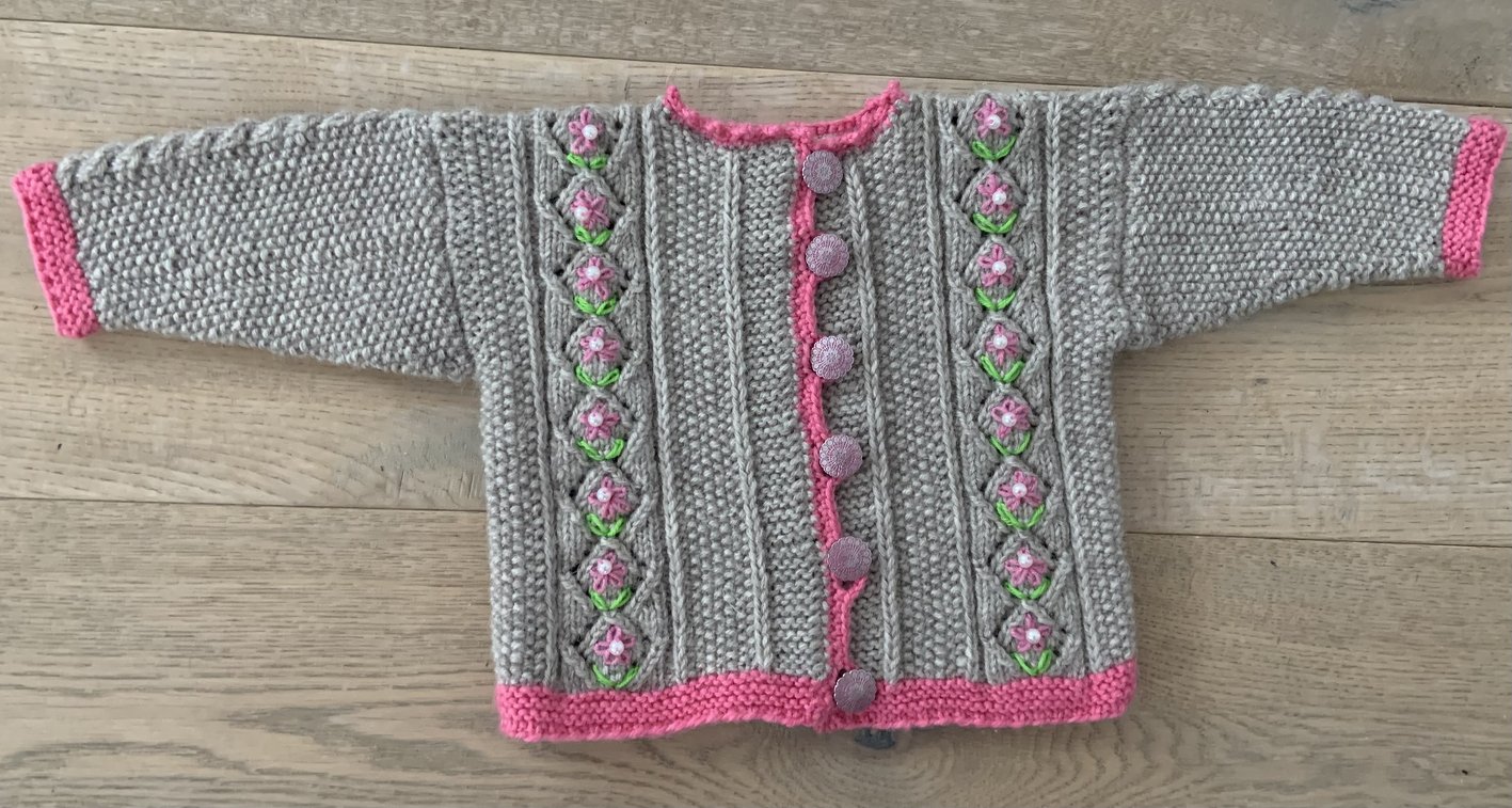 Gestrickte hellgraue Kinderjacke mit rosa Kanten, mittiger Knopfleiste und aufgenähten rosa Blüten an beiden Vorderseiten