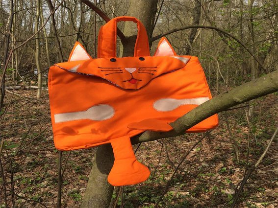 Leuchtend orange Katzenhandtasche mit Ohren, appliziertem Gesicht und Schwanz, hängt an einem Ast