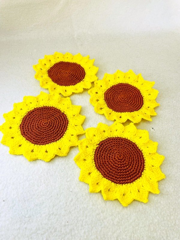 Vier gehäkelte Untersetzer in Sonnenblumenform auf hellem Untergrund