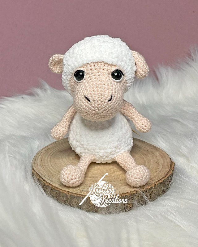 Gehäkeltes Osterlamm-Amigurumi auf Holzscheibe vor rosafarbenem Hintergrund
