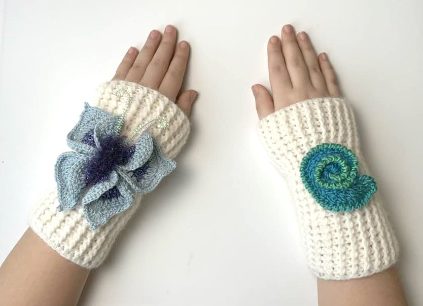 Fingerlose cremefarbene gehäkelte Handstulpen für Kinder, links mit blauer Blüte, rechts mit grüner Spirale