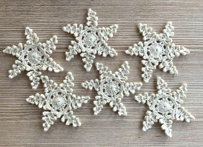 Sechs gehäkelte cremefarbene Schneeflocken auf Holzuntergrund