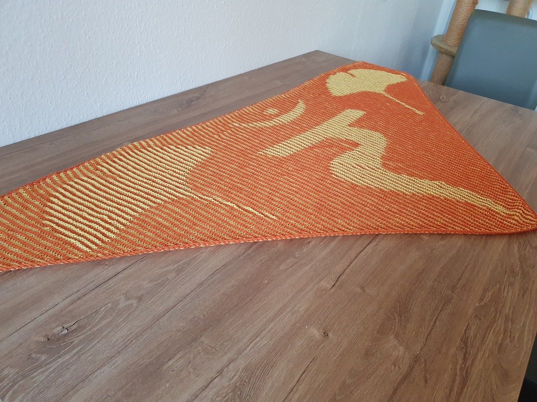Gestricktes dreieckiges Tuch mit Ginkgo-Blattmuster in Orange und Gelb auf einem Holztisch.