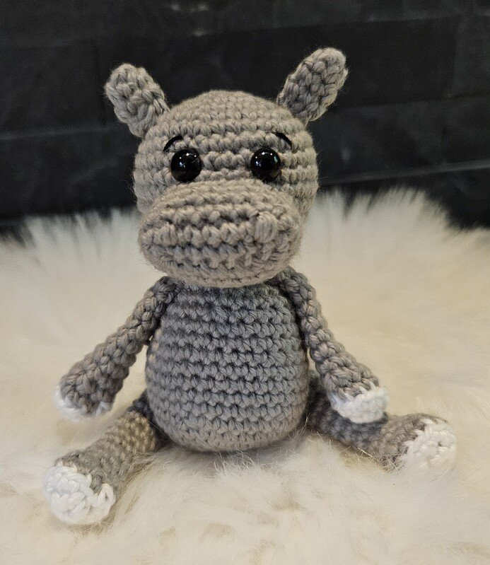 Nahaufnahme eines sitzenden gehäkelten Nilpferds mit sichtbaren Maschen und weißen Pfoten