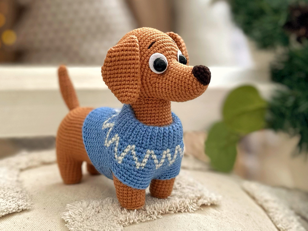 Brown crocheted dachshund amigurumi with blue sweater and white zigzag pattern