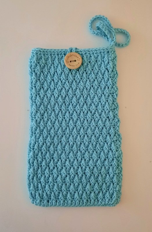 Hellblaue, handgehäkelte Hülle mit strukturiertem Muster, Schlaufe und rundem Holzknopf mit Gravur "handmade with love".