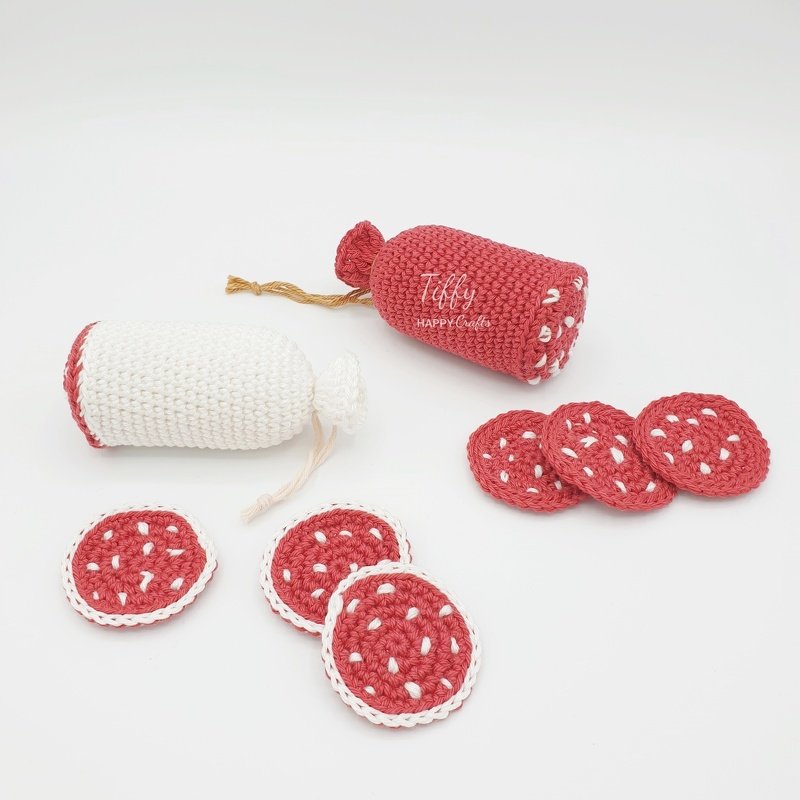 Two crocheted salami-style logs (one red, one white) with five round red crocheted slices featuring white flecks on a white background.
