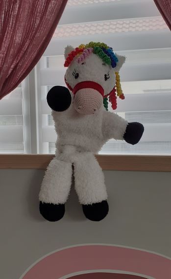 Weißes gestricktes Einhorn-Kuscheltier mit Regenbogenmähne auf Fensterbank