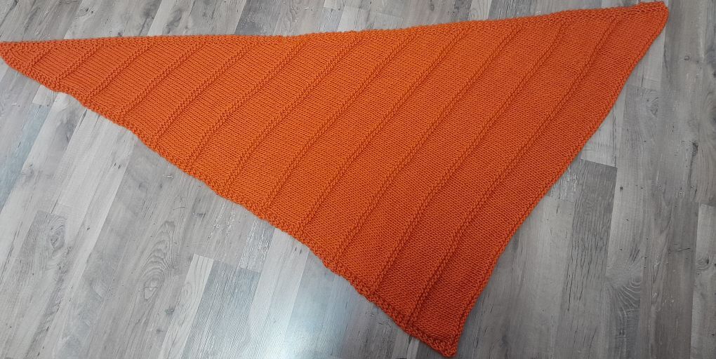 Gestricktes orangenes Dreieckstuch mit diagonalem Rippenmuster auf hellem Holzboden