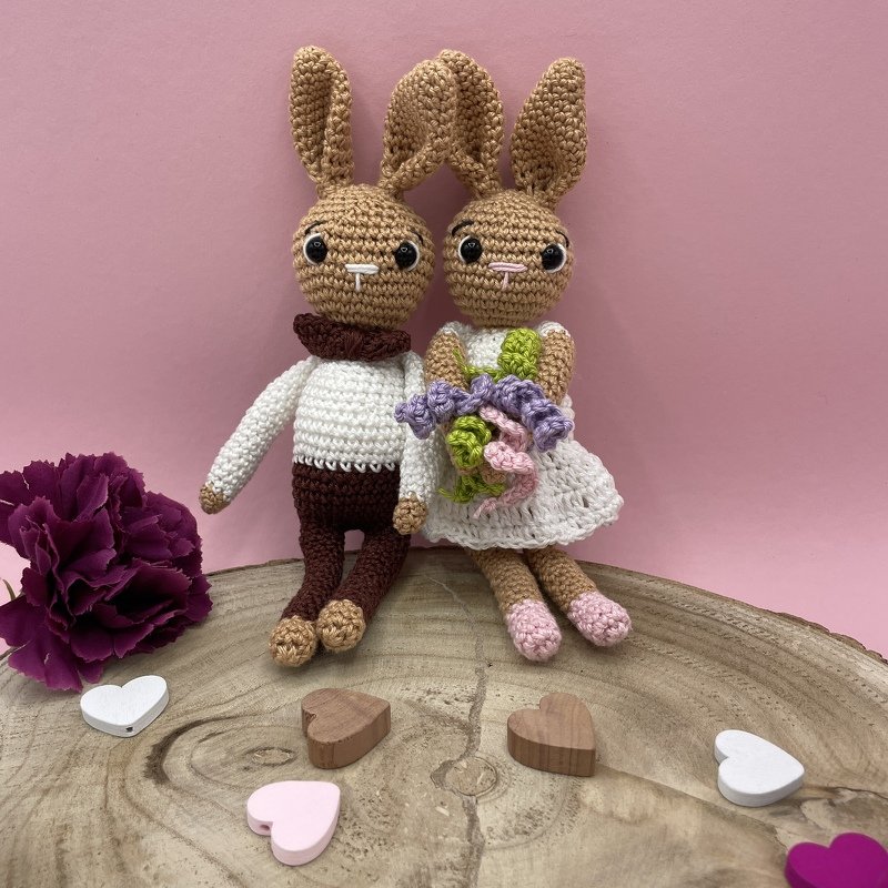 Crocheted amigurumi bunny bride and groom sitting on a wooden slice