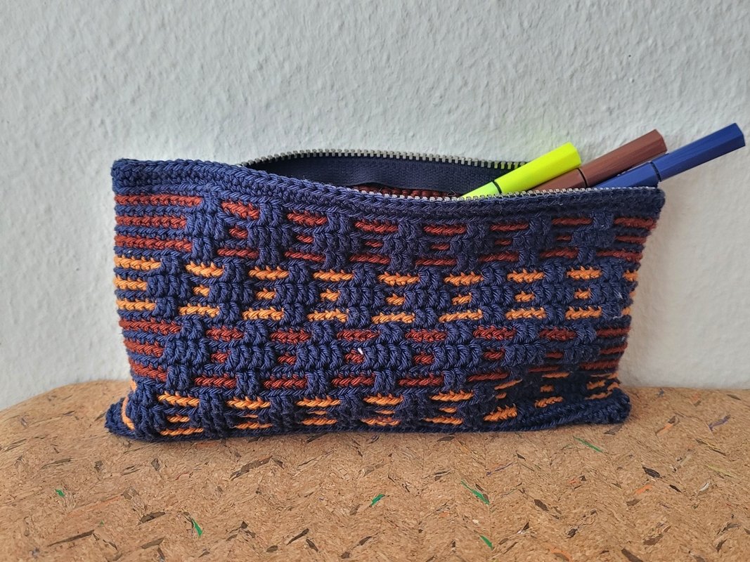 Kleines gehäkeltes Etui in Dunkelblau mit orange-braunen Streifen, geöffnet und mit Stiften gefüllt