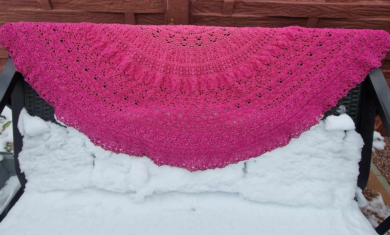 Fuchsiafarbenes halbrundes Häkeltuch über schneebedeckter Bank, kontrastreicher Hintergrund