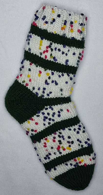 Gestrickte Socke weiß mit bunten Noppen und dunkelgrünen Streifen