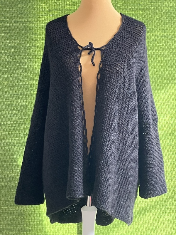 Dunkle, weit geschnittene Häkeljacke für Damen mit Bindeband am Ausschnitt auf einer Schneiderpuppe.