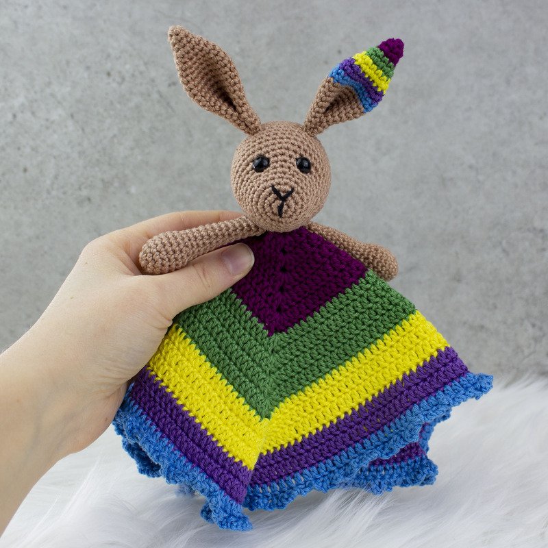 Gehäkeltes Schnuffeltuch mit Hasenkopf und buntem Chevronmuster, von einer Hand gehalten