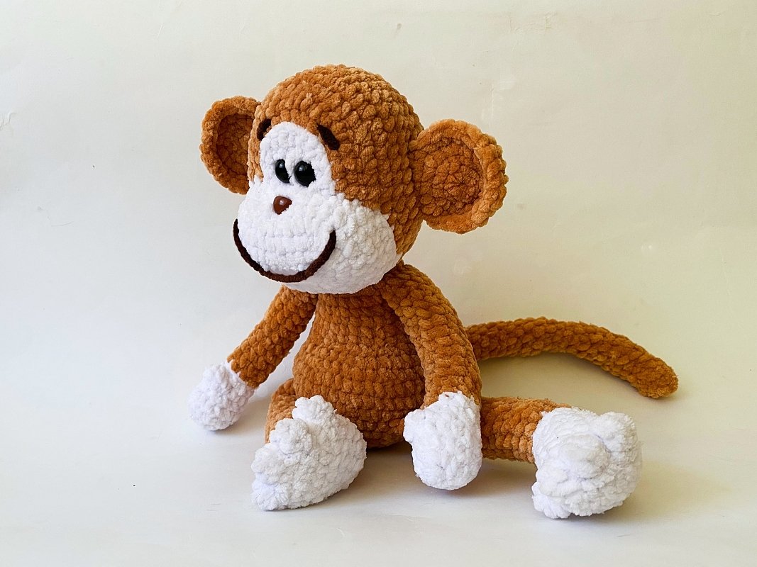 Brown and white crocheted amigurumi monkey toy seated with long tail