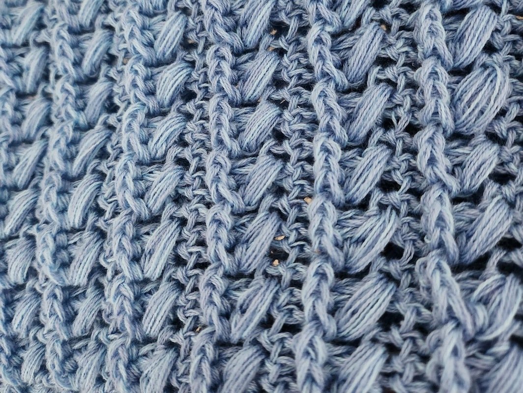 Nahaufnahme hellblauen Häkelstoffs mit Reliefmaschen und diagonaler Struktur.