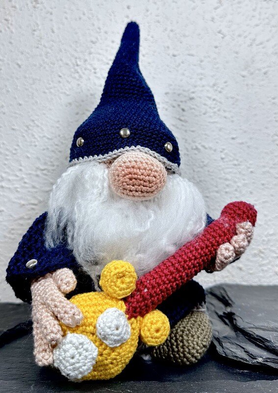 Gehäkelter Wichtel mit blauer Mütze, weißem Bart und rot-gelber Gitarre