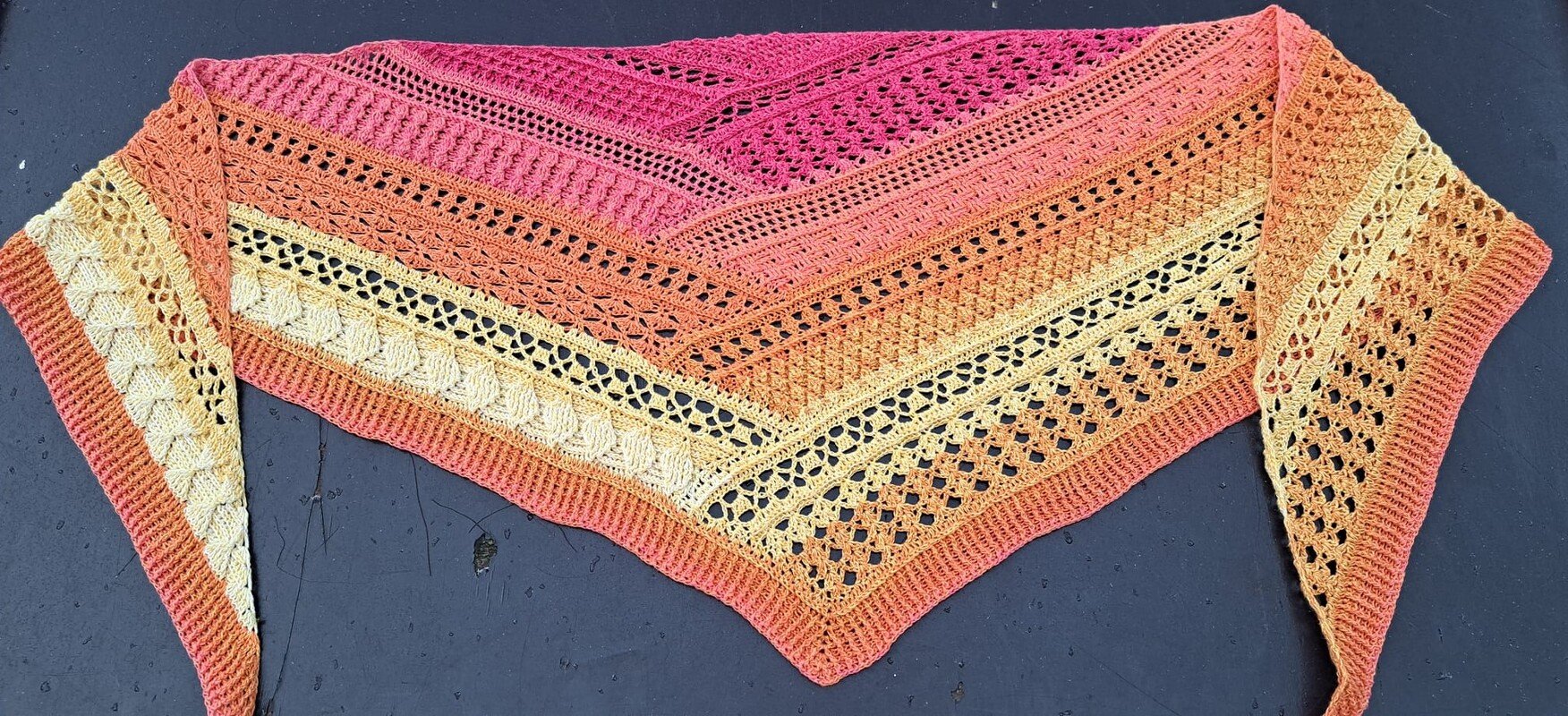 Crocheted triangle shawl with ombre pink, orange and yellow bands showing several distinct stitch textures.